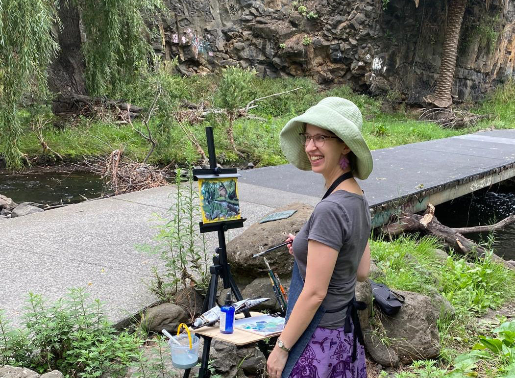 Woman painting outdoors by a stream with a nature setting